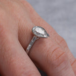 Load image into Gallery viewer, Closeup of the ring showing the bezel setting for the pear diamond and the baguette accent diamonds in channel setting.