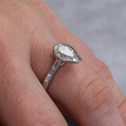Closeup of the ring showing the bezel setting for the pear diamond and the baguette accent diamonds in channel setting.