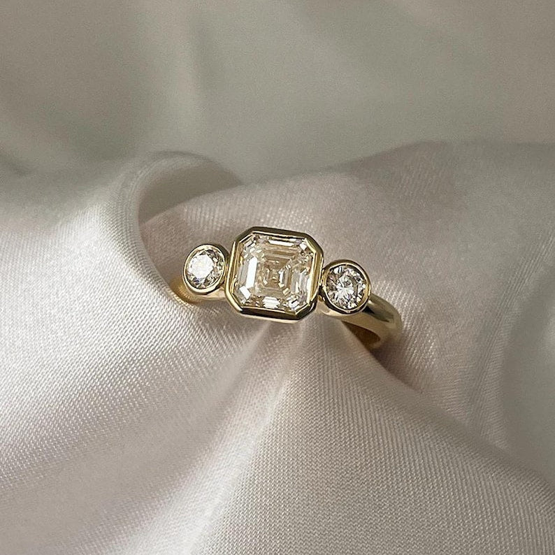 Asscher Cut Trilogy Diamond Engagement Ring featuring a 1.5ct IGI Certified Asscher Cut Lab Grown Diamond with round lab grown diamond side stones in solid gold. Three-stone engagement ring with 1.82ct total carat weight.
