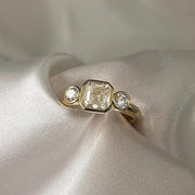 Asscher Cut Trilogy Diamond Engagement Ring featuring a 1.5ct IGI Certified Asscher Cut Lab Grown Diamond with round lab grown diamond side stones in solid gold. Three-stone engagement ring with 1.82ct total carat weight.