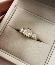 Asscher Cut Trilogy Diamond Engagement Ring featuring a 1.5ct IGI Certified Asscher Cut Lab Grown Diamond with round lab grown diamond side stones in solid gold. Three-stone engagement ring with 1.82ct total carat weight.